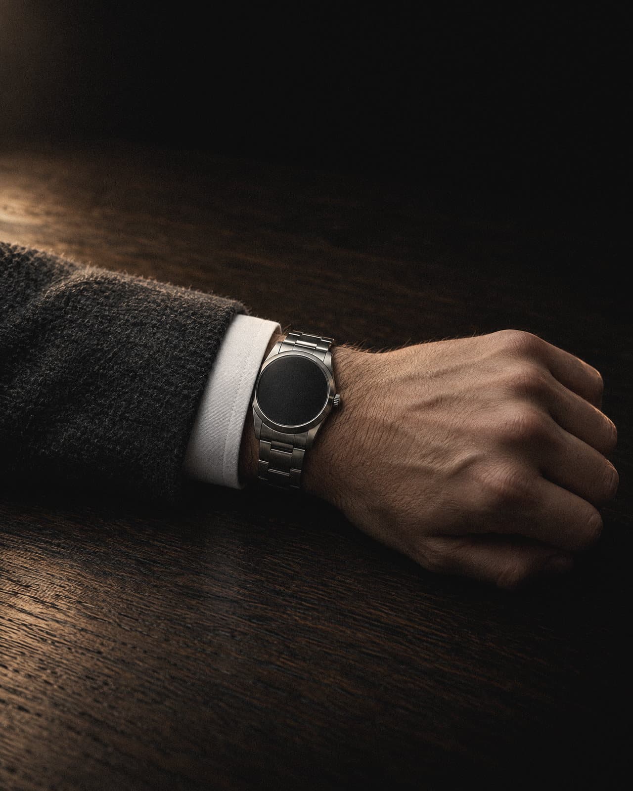 The founder, in detail: a hand and a watch resting on the oak table