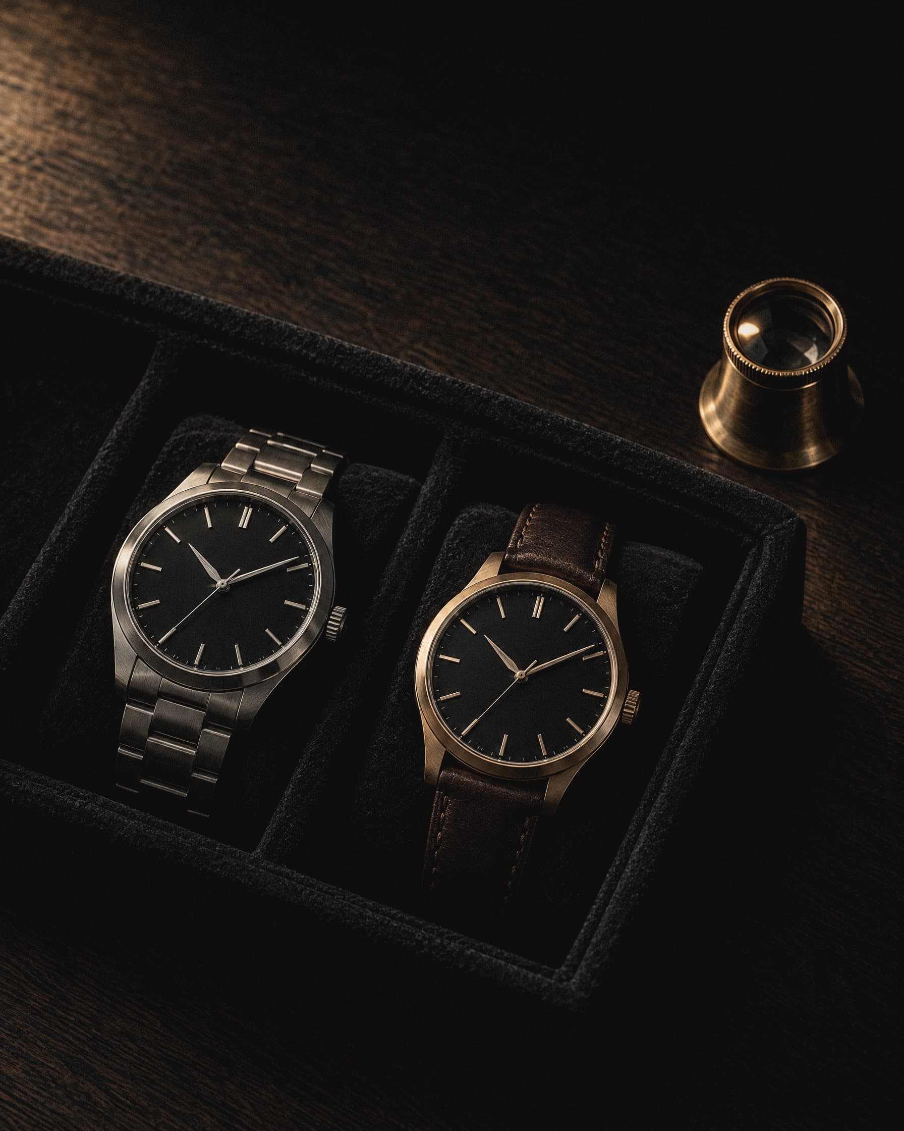 Two watches on a velvet tray beside a jeweller's loupe